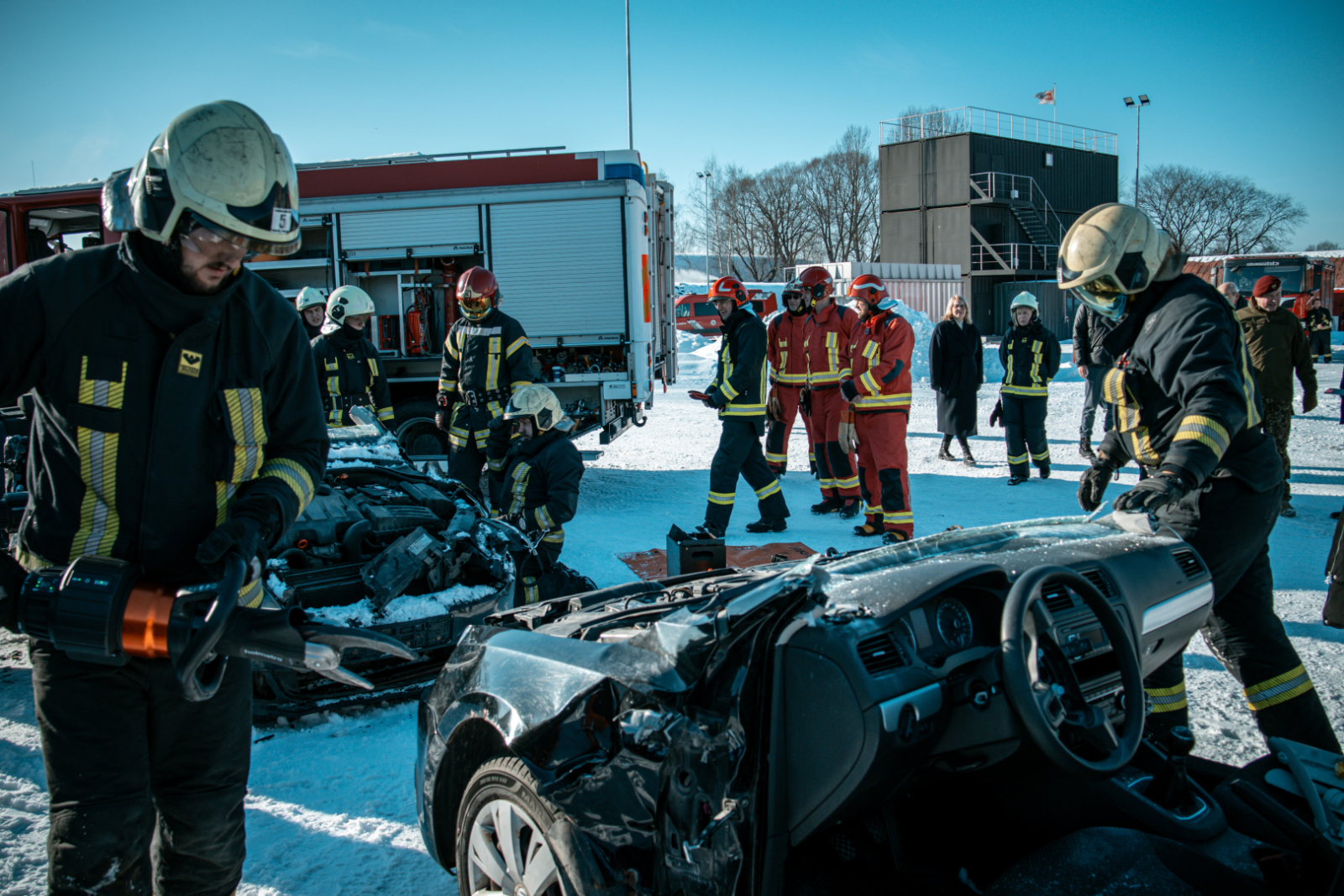 Sniegots koledžas praktisko mācību poligons. Tajā vairāki ugunsdzēsēji glābēji ap bojātām automašīnā. Fonā ugunsdzēsības automašīna.