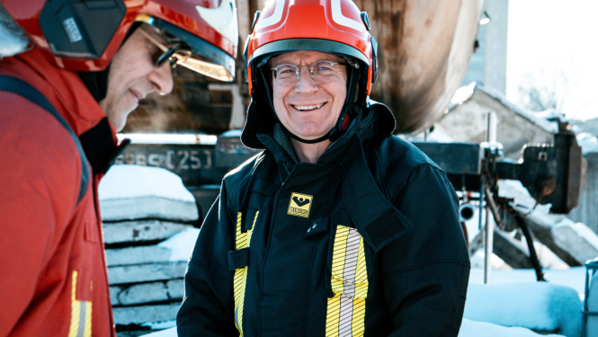 Valsts prezidents Edgars Rinkēvičs stāv ārā sniegotā teritorijā, smaida. Viņam uzvilkts ugunsdzēsēja glābēja formas tērps.
