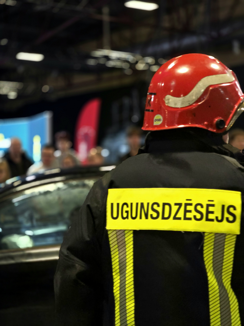 Ugunsdzēsējs glābējs no mugurpuses, fonā izstādes telpa.