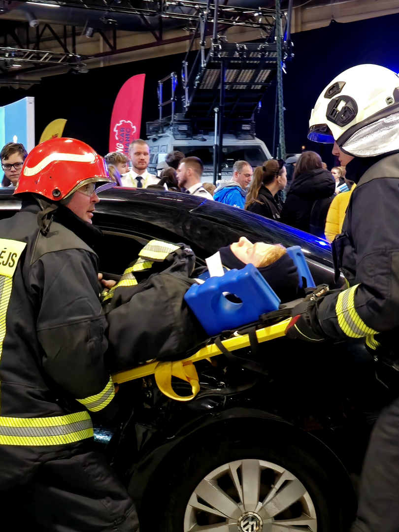 Divi ugunsdzēsēji glabēji nest kolēģi uz nestuvēm. Tiek veikts paraugdemonstrējums glābšanas darbiem, kas saistīti ar ceļu satiksmes negadījumu. 