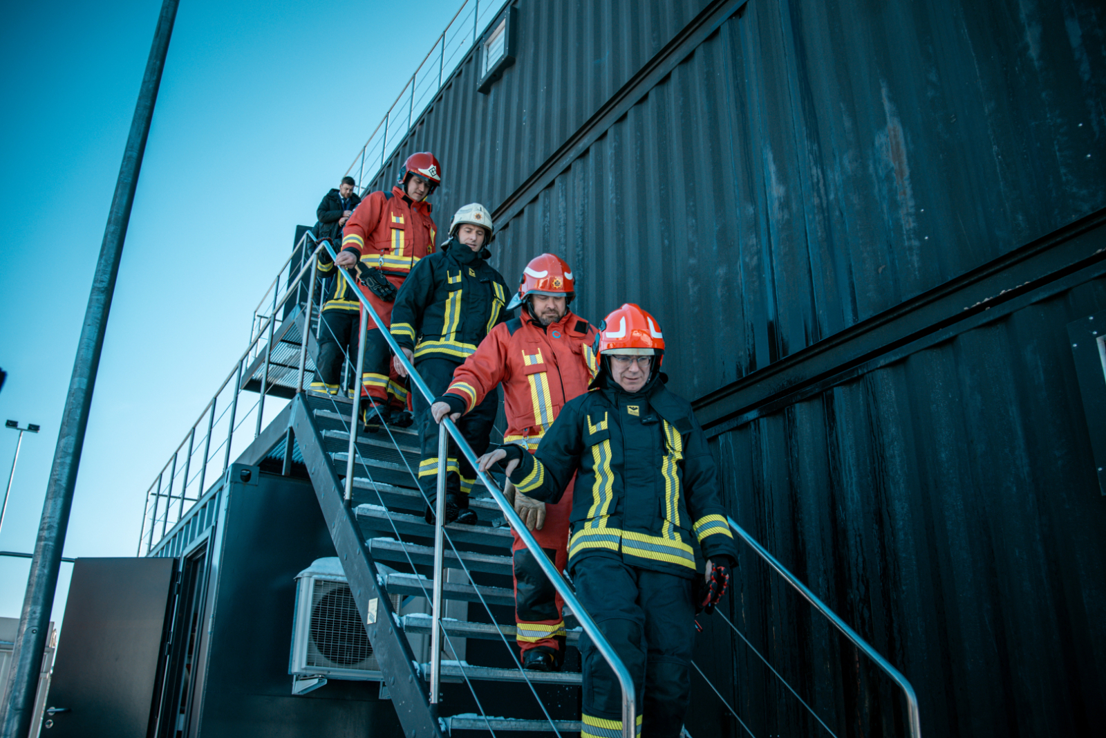 Valsts prezidents Edgars Rinkēvičs un koledžas pārstāvji kāpj lejup pa kāpnēm, kas atrodas pie ēkas ārsienas.